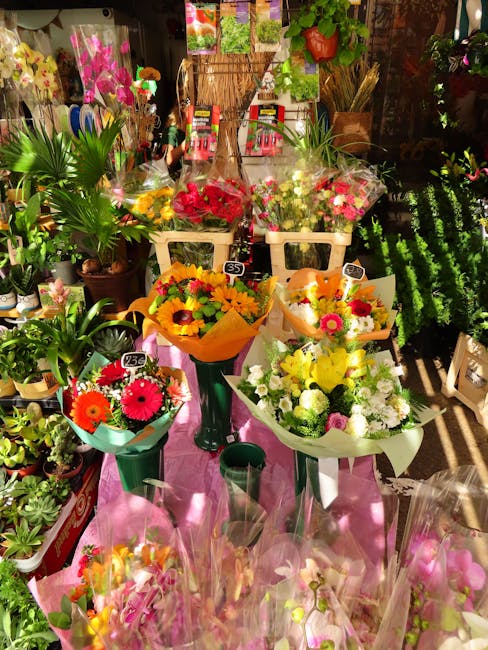 A vibrant floral display from flowersnorthharrow.co.uk showcasing an assortment of fresh bouquets arranged on a white table with pink fabric, surrounded by potted green plants and flower displays. The