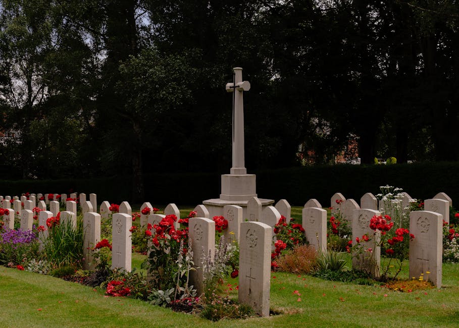 A serene cemetery scene featuring a well-maintained graveyard with white headstones arranged in neat rows, surrounded by vibrant red and purple flowers, including roses and petunias, planted in the so