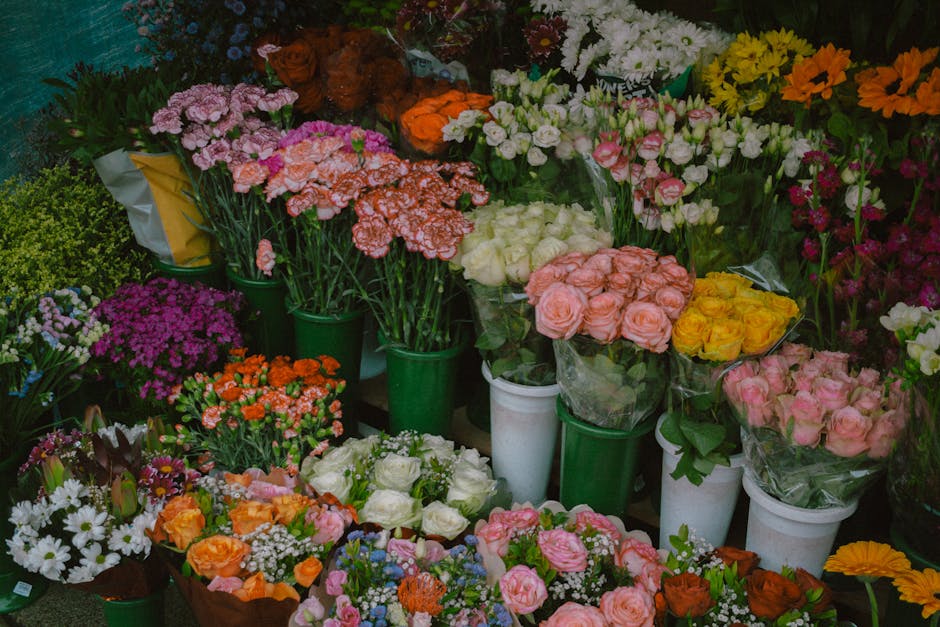 An array of fresh flower bouquets and potted floral arrangements displayed on a shop table, featuring a variety of vibrant colours including pink, orange, yellow, white, and purple. The bouquets inclu