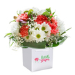 Radiating joy and sincerity, this fresh bouquet shines upright in a stylish white gift bag-an ideal surprise for any occasion in North Harrow, from a cheerful birthday near Shaftesbury Avenue to an impromptu thank you after a morning in Headstone Manor Recreation Ground. Coral and peach carnations, with their characteristic layered, soft petals, blend beautifully with crisp white daisies punctuated by green-yellow centers, channeling the uplifting spirit of an early spring day. Dainty sprays of baby's breath lend a whimsical, airy accent, while a few purple-tinged buds peep shyly among the blooms, adding intrigue and soft contrast. Nestled at the base, broad glossy leaves create a verdant, supportive wrap, completing the rounded, abundant silhouette that marks a bouquet crafted with care. The understated white bag-fitted with sturdy ribbon handles-frames the flowers, emphasizing their freshness and elegance. Each blossom is thoughtfully placed, inviting the recipient to pause, breathe in hints of subtle sweetness, and feel genuinely celebrated. This arrangement is more than just a floral gift-it's a reflection of local pride and heartfelt artistry from the heart of North Harrow.